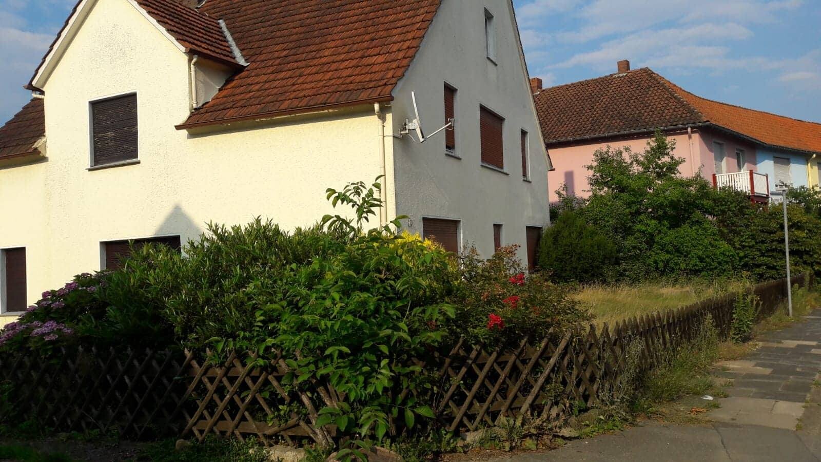 Bunte Häuserzeile mit gelben, grauen und rosa Fassaden, Holzzaun und Grünflächen am Gehweg