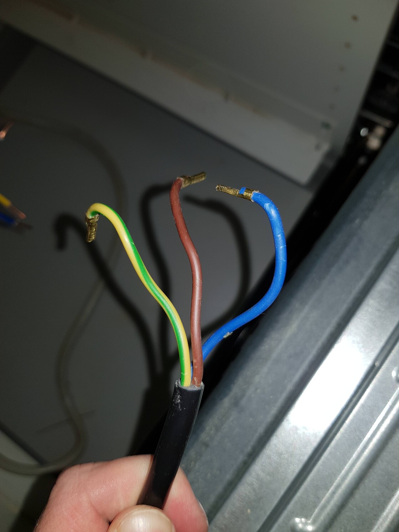 Hand hält abisolierte braune blaue und grün-gelb Kabel in Haustechnik-Installation