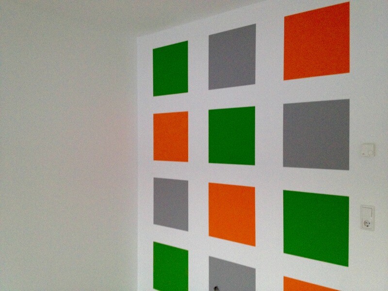 Weiße Wand mit Anordnung von grünen, orangenen und grauen Quadraten