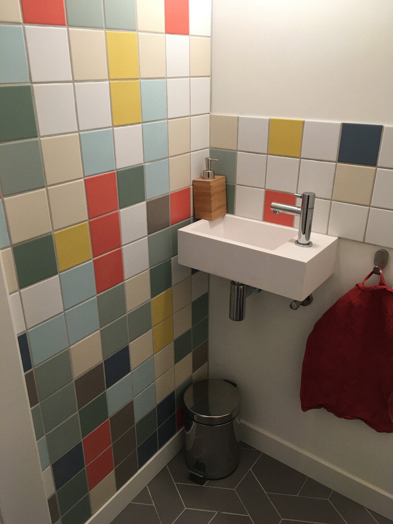 Kleines Bad mit bunten Fliesen, Waschbecken, Metallarmatur, Seifenspender und rotem Handtuch