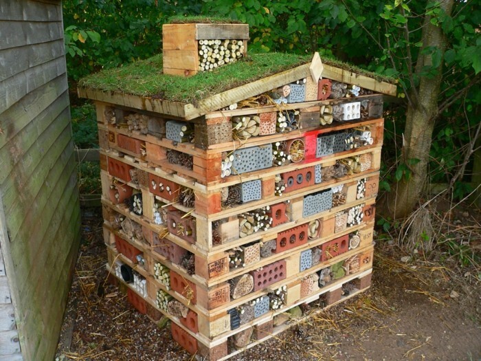 Insektenhotel aus Paletten mit Gründach, Röhren und Lochplatten im Garten.