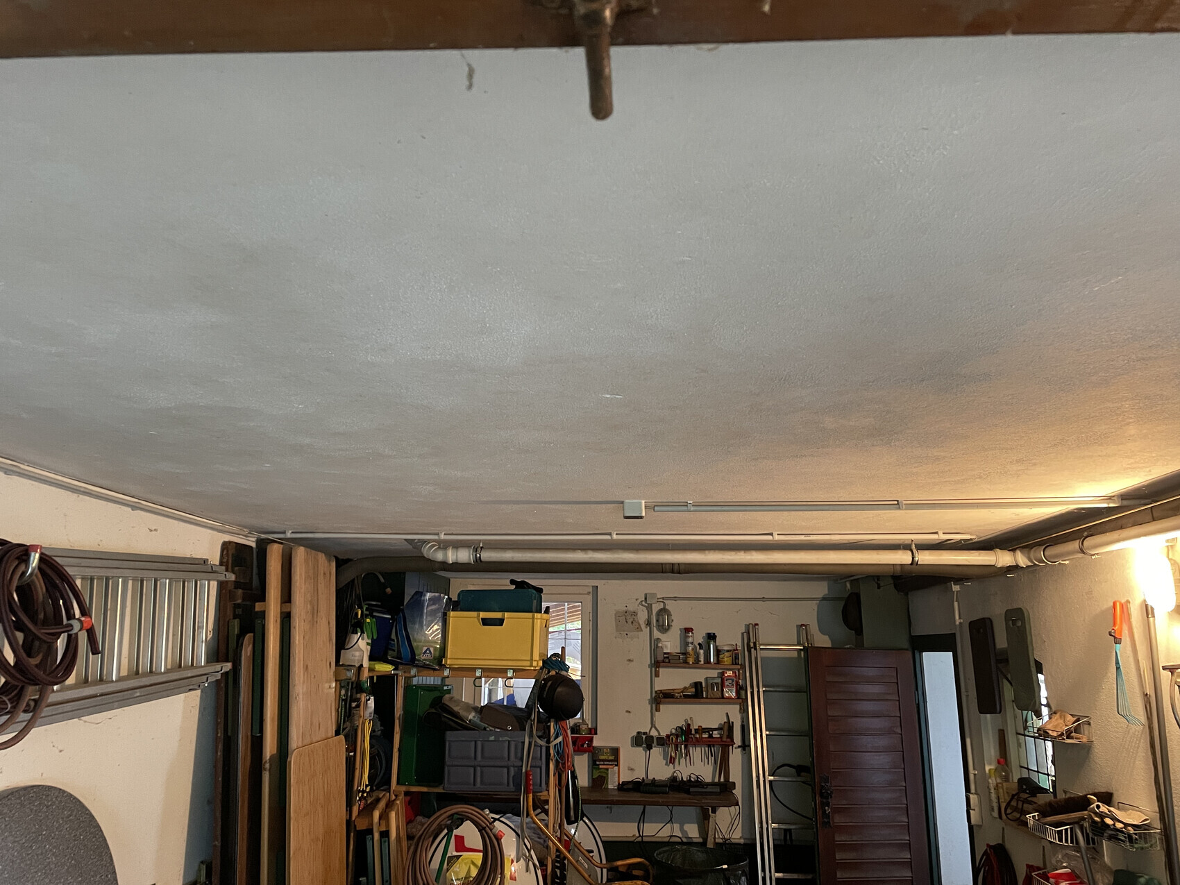 Unordentliche Garage/Werkstatt mit Regalen, Werkzeugen, Schläuchen, Kisten und Beleuchtung.