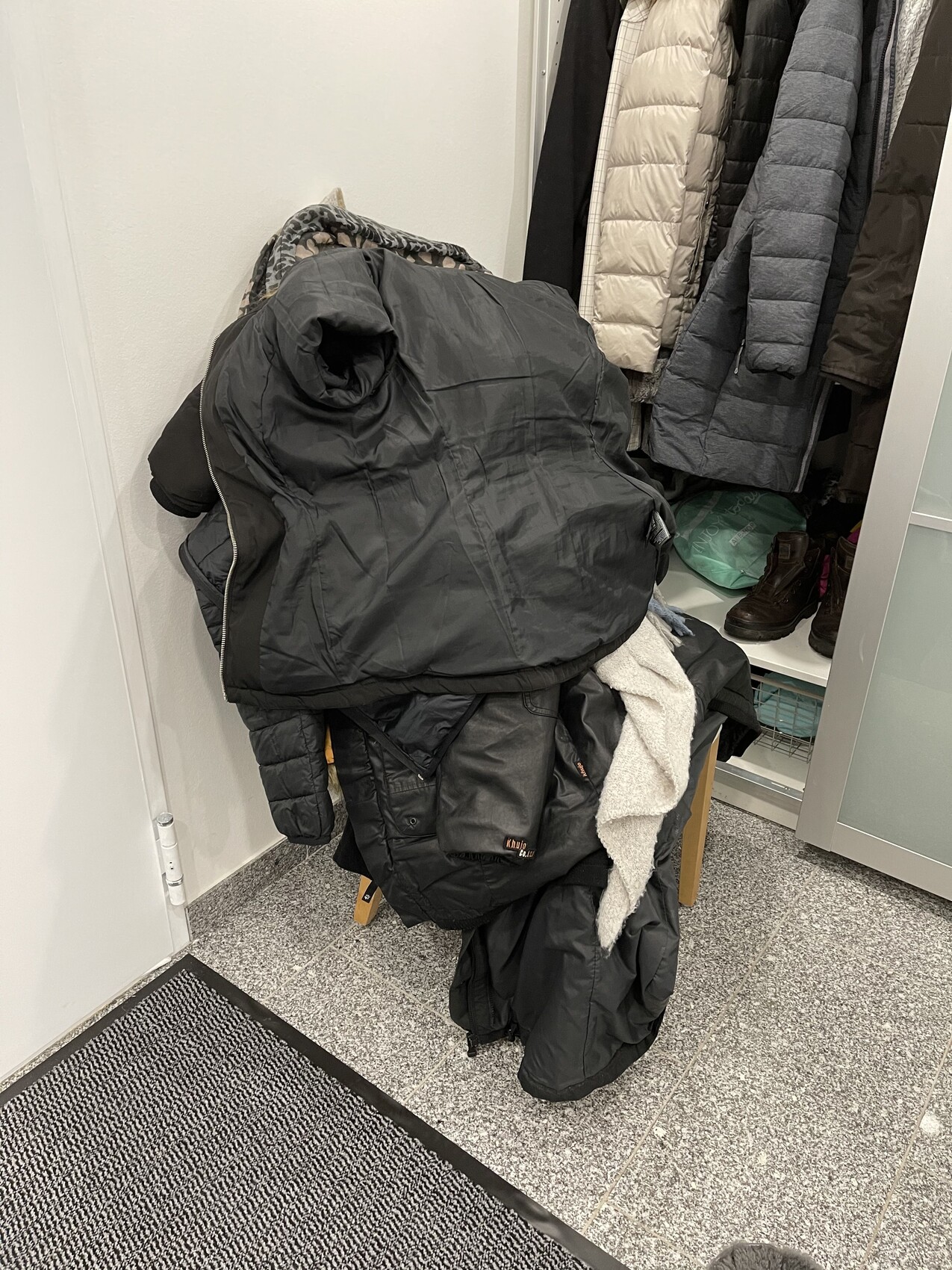 Große schwarze Daunenjacke liegt auf einem Stuhl in der Garderobe, daneben hängen weitere Jacken.