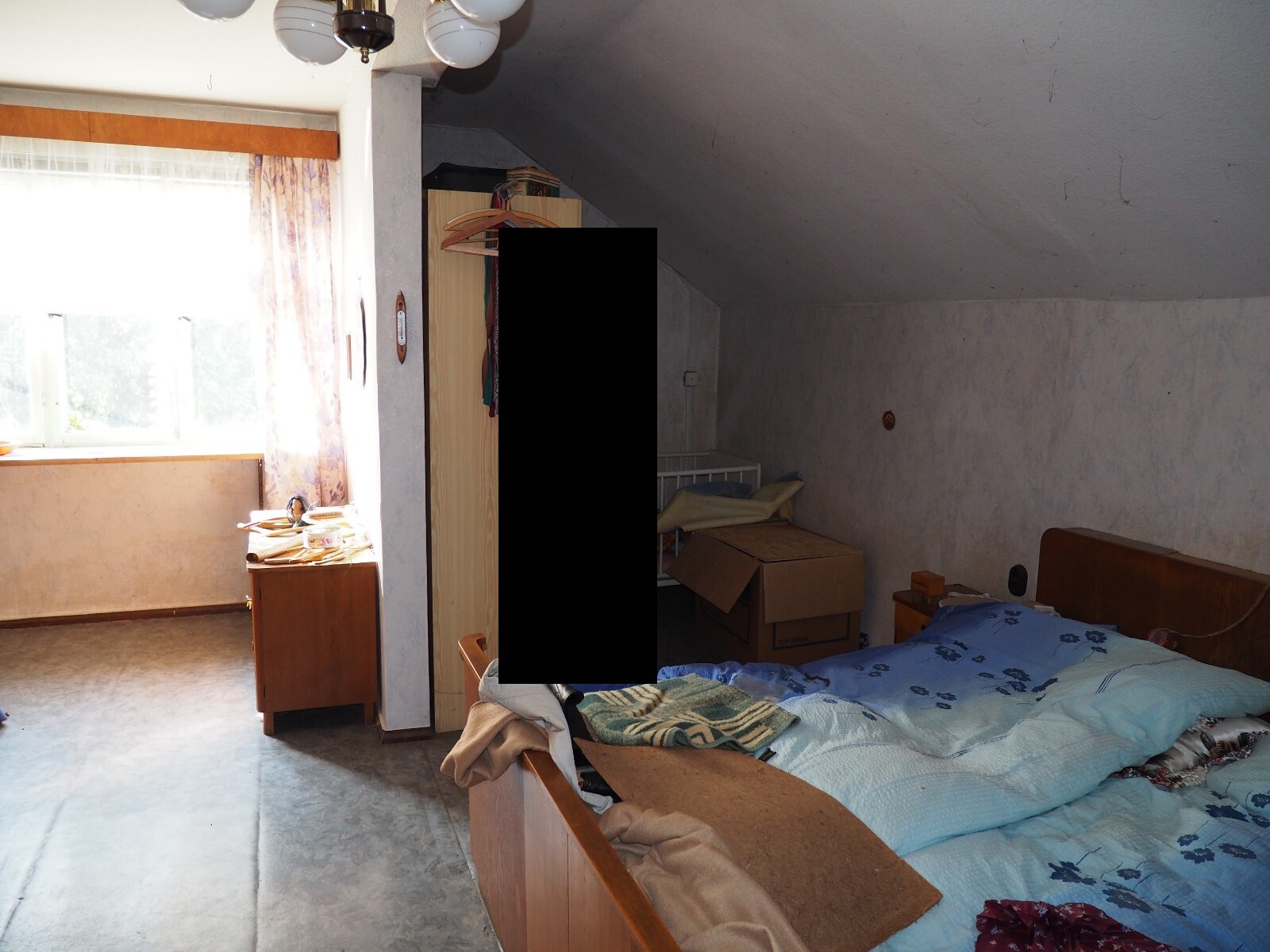 Dachgeschoss-Schlafzimmer: Bett rechts, unordentliche Ecke mit Kartons und Kleidung, Fenster links.