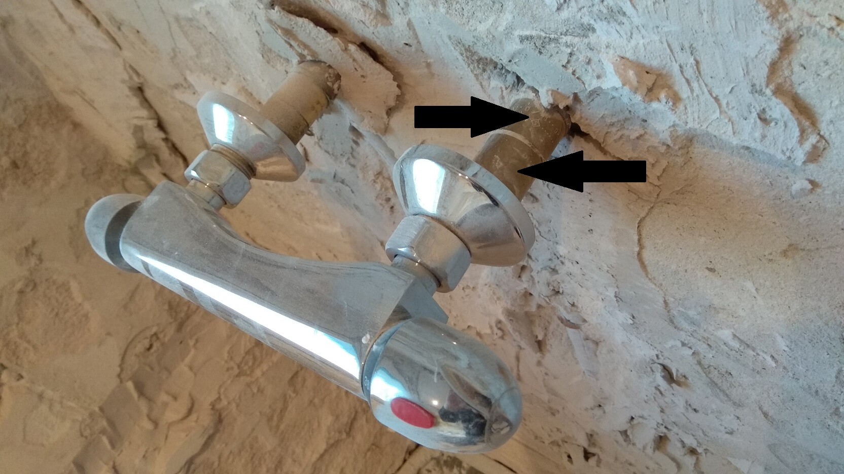 Chromarmatur mit zwei Ventilen an rauer Wand im Rohbau eines Badezimmers.