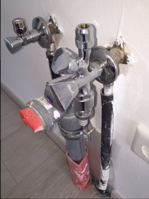 Mehrere Chrom-Absperrventile und Rohre einer Sanitärinstallation hinter einer Wand.