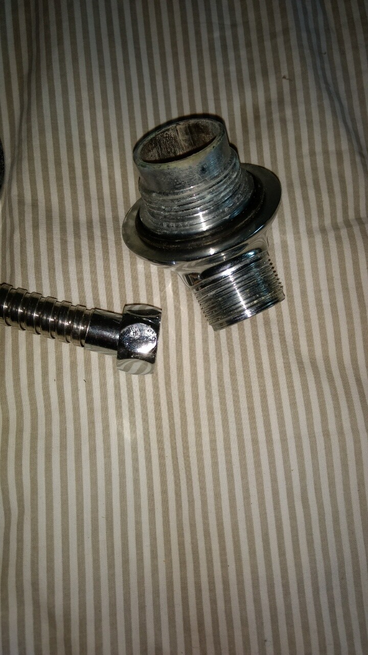 Zwei verchromte Metallbauteile: ein Gewinde-Adapter und ein flexibler Schlauch auf Stoffhintergrund.