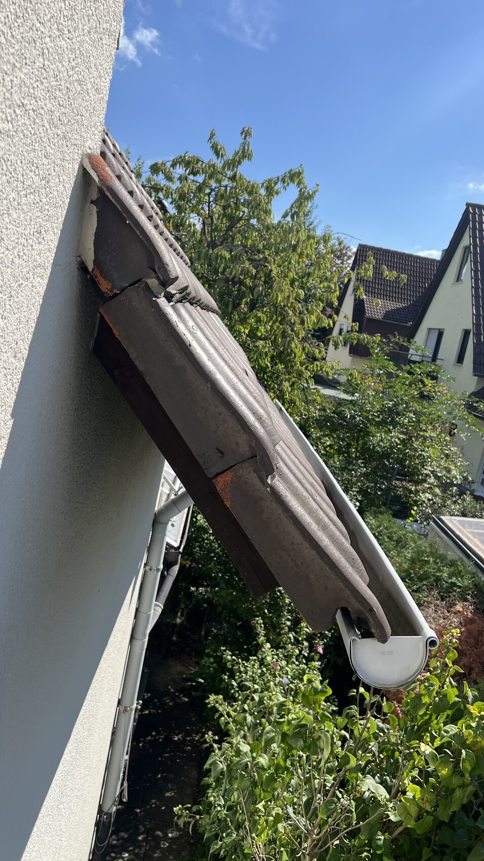 Nahaufnahme eines geneigten Daches mit Dachziegeln, Dachrinne und angrenzender Fassade.