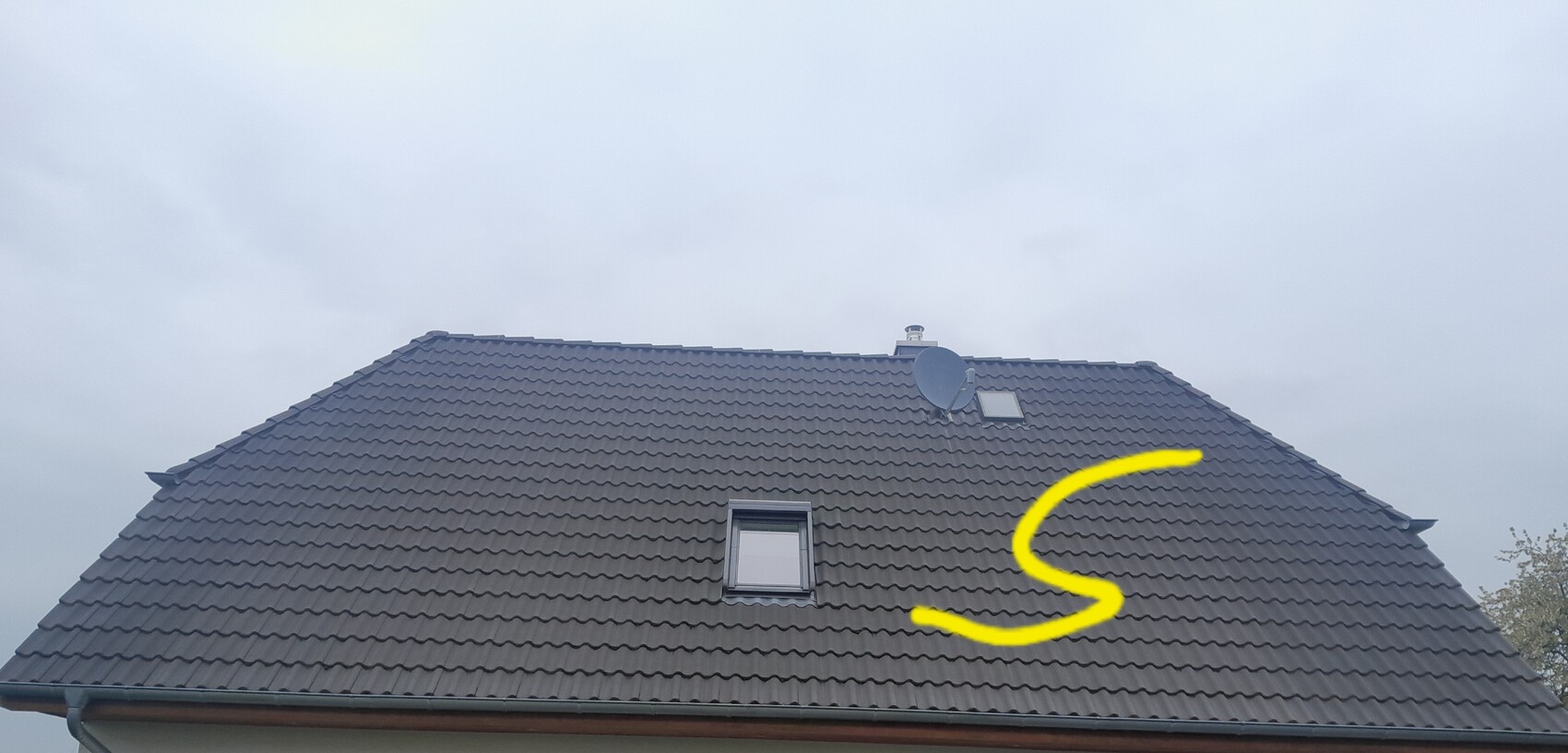 Dach eines Hauses mit grauen Ziegeln, Dachfenster und Satellitenschüssel; gelb markierte S-Form auf dem Dach.