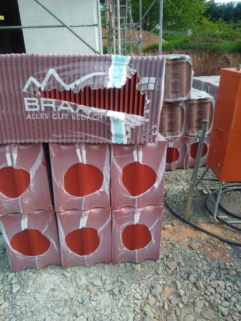 Stapel roter Kartons mit runden Öffnungen, Baugerüst und Kies auf einer Baustelle.