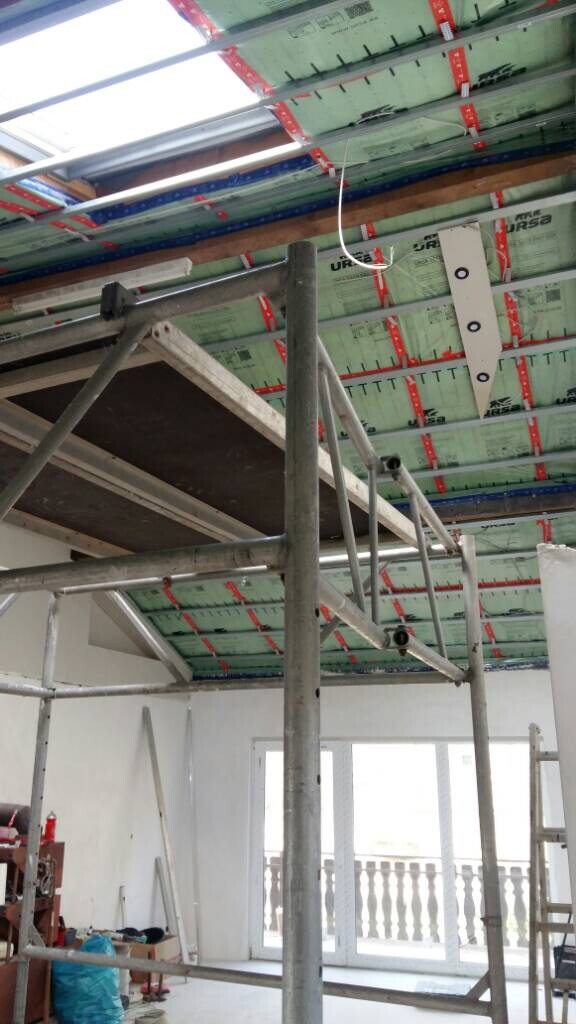 Innenraum einer Baustelle mit Metallgerüst, grün isolierter Decke und Fensterblick nach außen