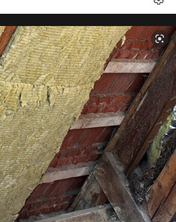 Dachkonstruktion mit gelber Daemmung zwischen Holzbalken und Backsteinwand