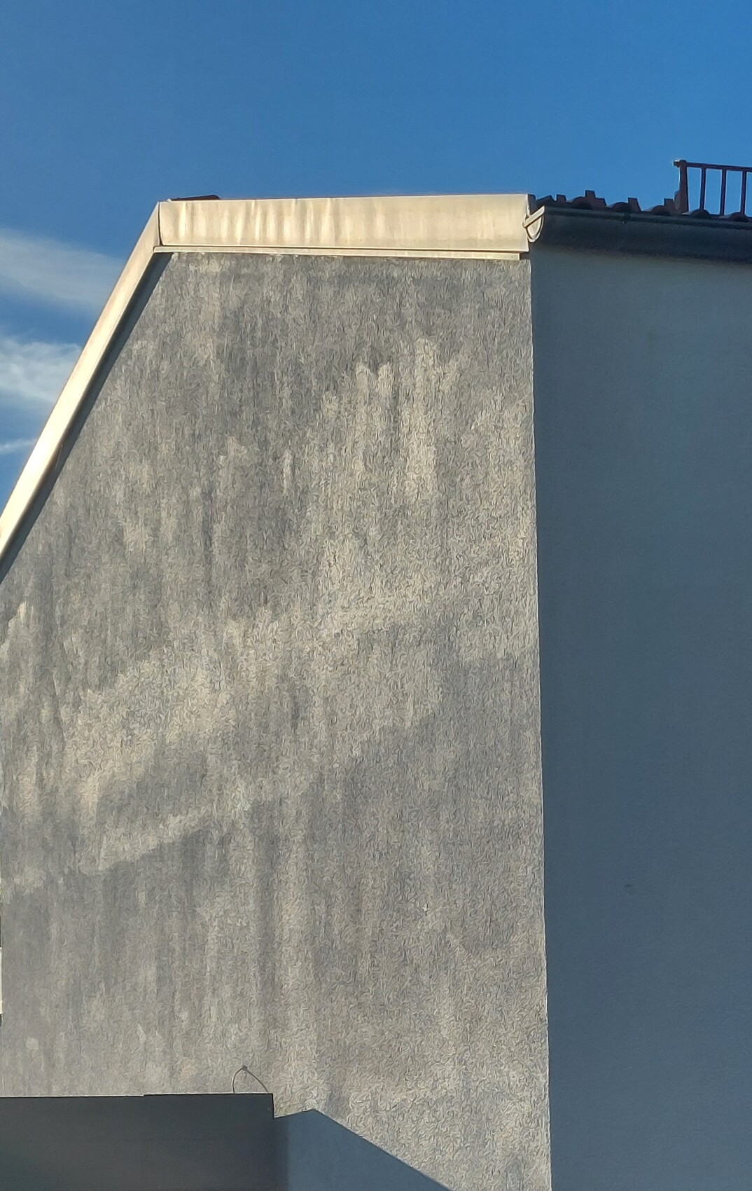 Außenwand mit schräger Dachkante und heller Dachrand vor blauem Himmel.