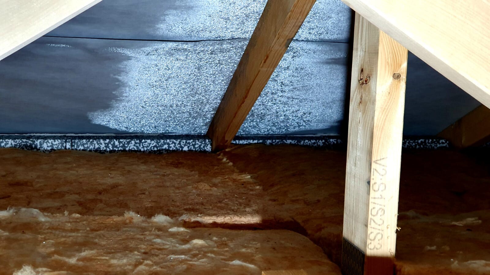 Dachboden mit Holzsparren, vertikalem Balken und brauner Dämmung, blau-grauer Dachunterbau.