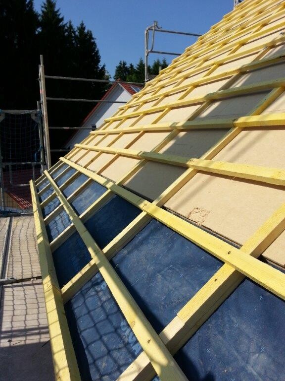 Dachkonstruktion mit Holzlatten auf Unterlage und Baugerüst im Hintergrund