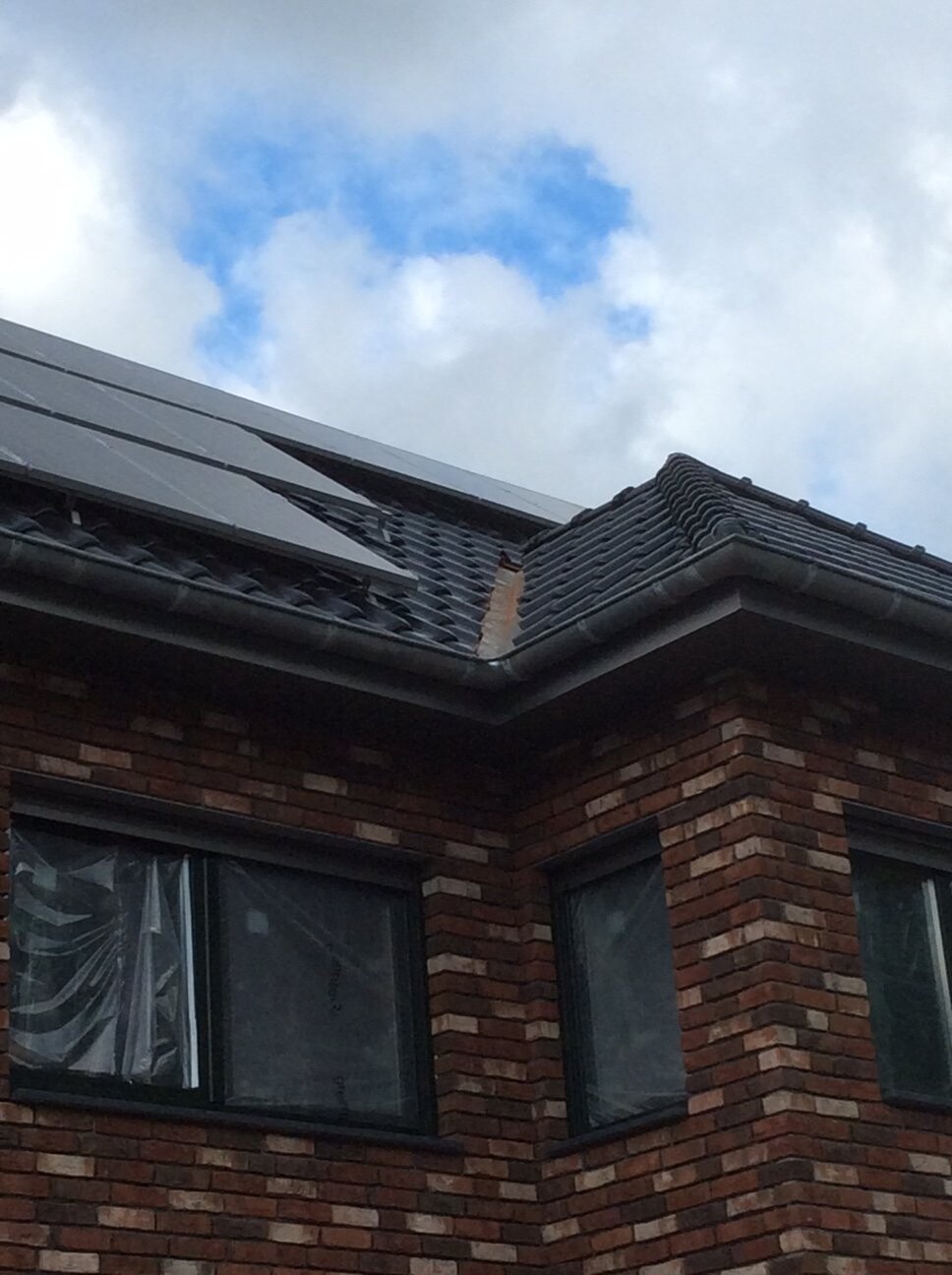 Außenansicht eines Backsteinhauses mit Ziegeldach und Solaranlage unter Wolken