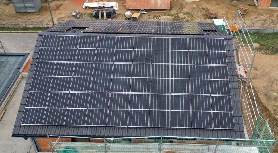 Dach eines Hauses mit dicht installierten Solarmodulen; Baugerüst und Baustelle im Hintergrund.