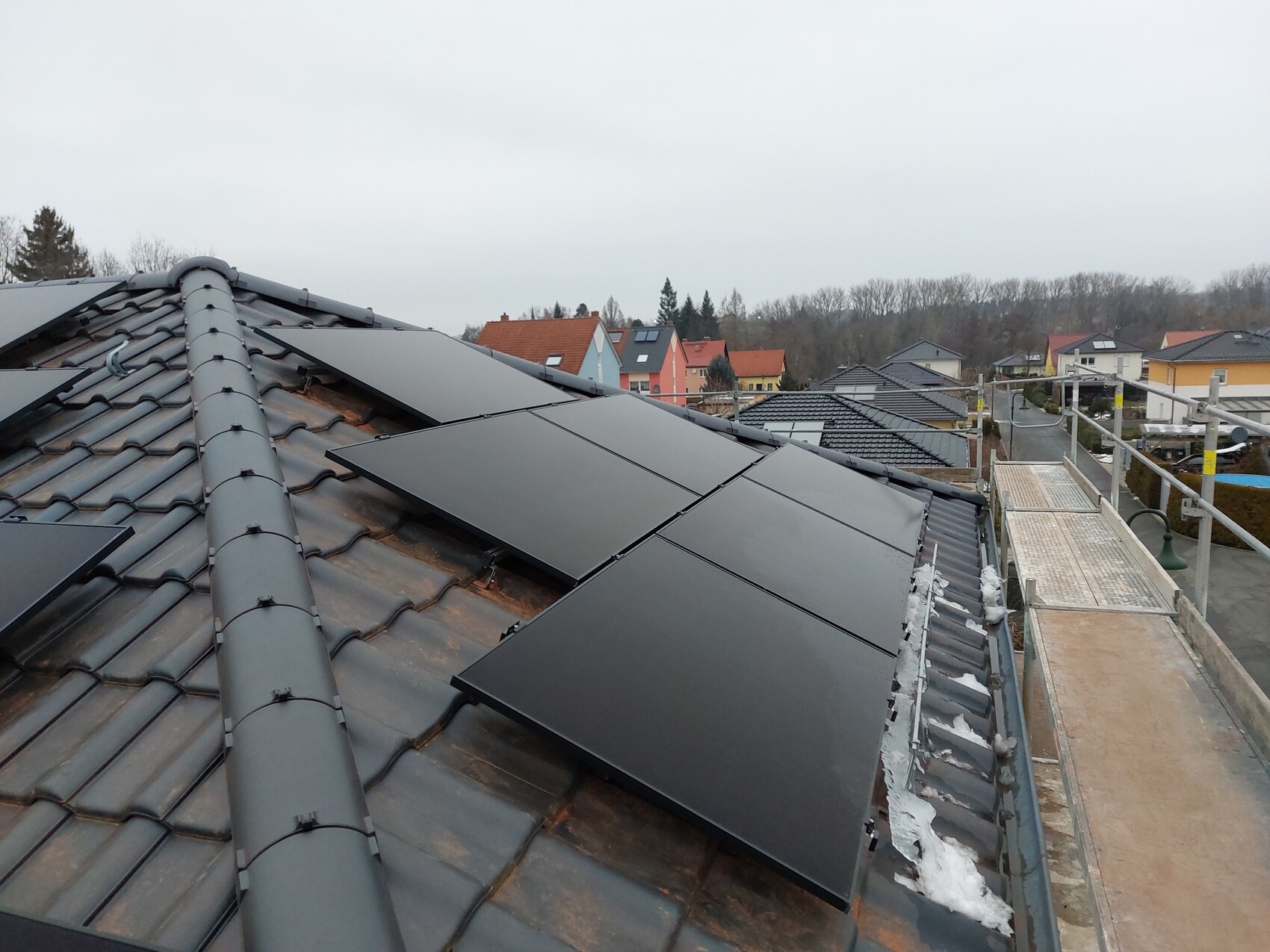 Dach mit schwarzen Solarmodulen auf Ziegeln; angrenzende Häuser, Baugerüst rechts.