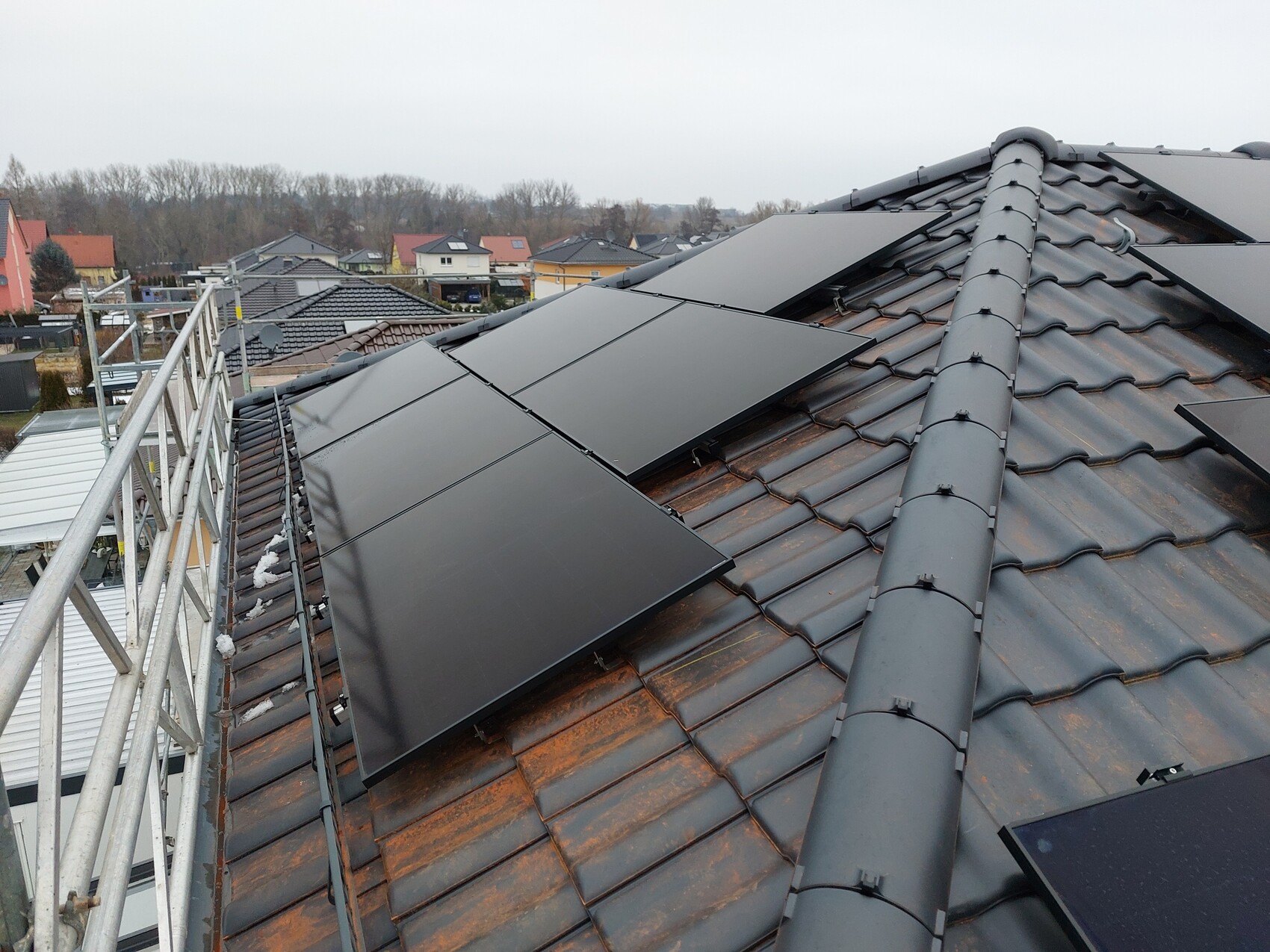 Solarmodule auf braunem Ziegeldach, Gerüst am Rand, Blick auf Nachbarhäuser.