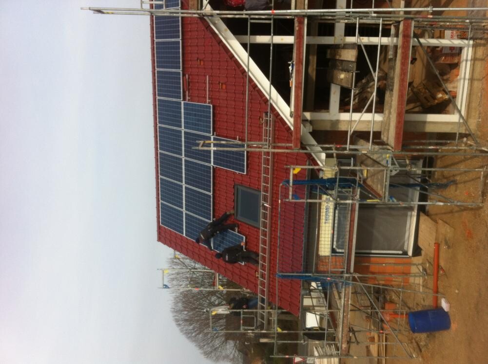 Baustelle mit rotem Dach, Solarpanelen installiert und Gerüst um das Gebäude.