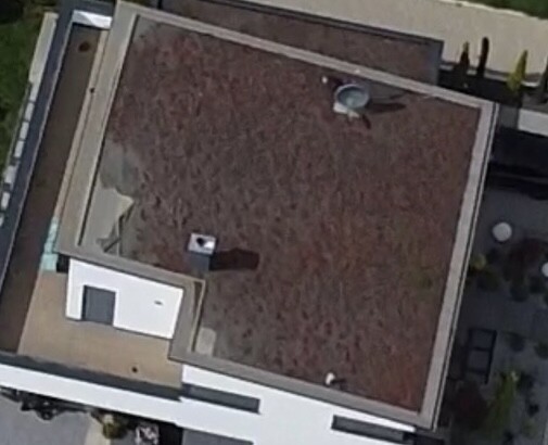 Luftaufnahme eines braunen Flachdachs mit kleinem Anbau und Satellitenschüssel.