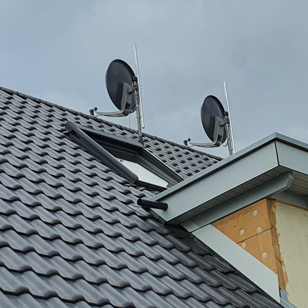Dach mit grauen Ziegeln, Dachfenster und zwei Satellitenschüsseln auf dem Dach.
