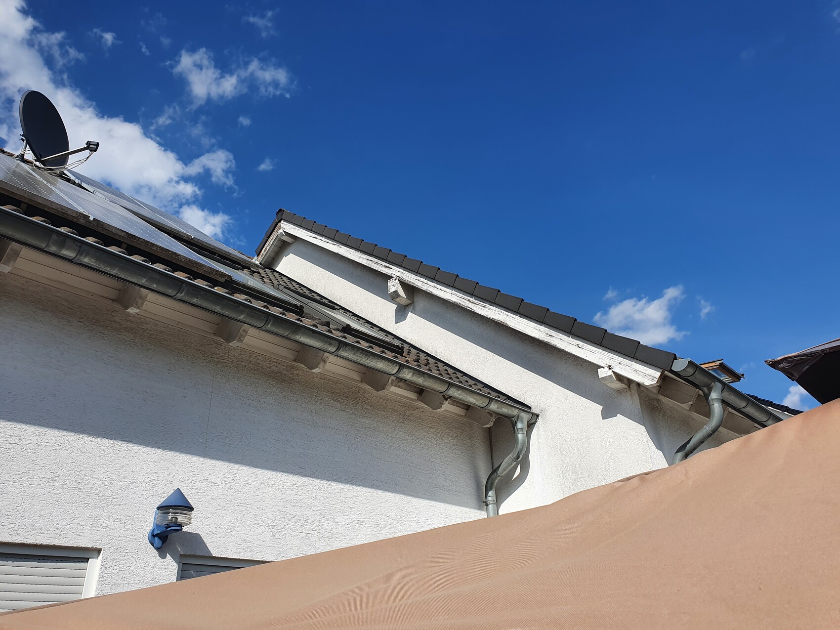 Dach eines weißen Hauses mit Satellitenschüssel, Dachrinne und blauem Himmel.