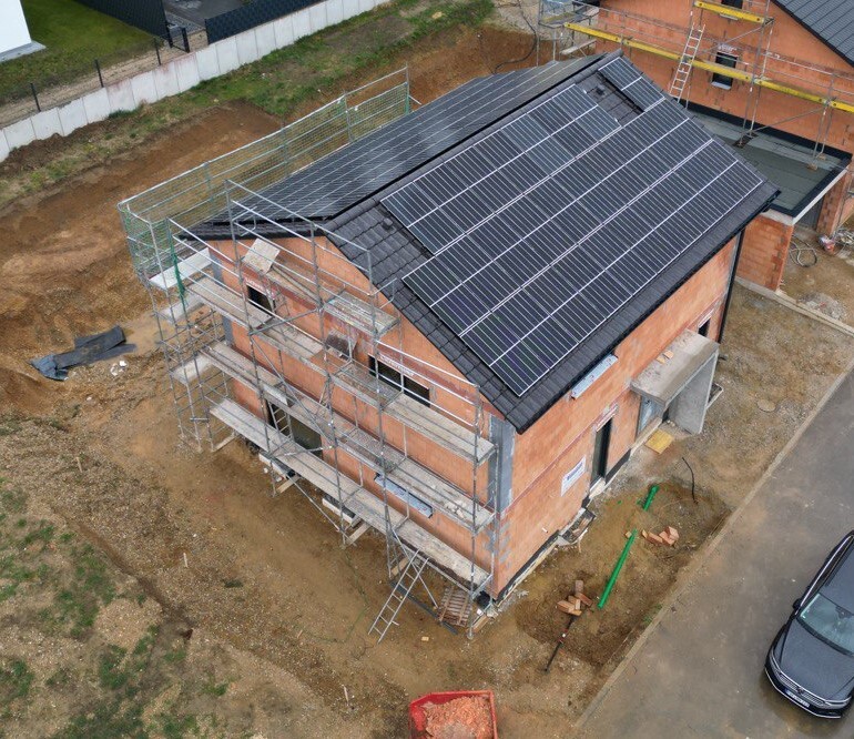 Neues zweigeschossiges Haus mit Solarpaneel-Dach und Baugerüst um die Fassade.