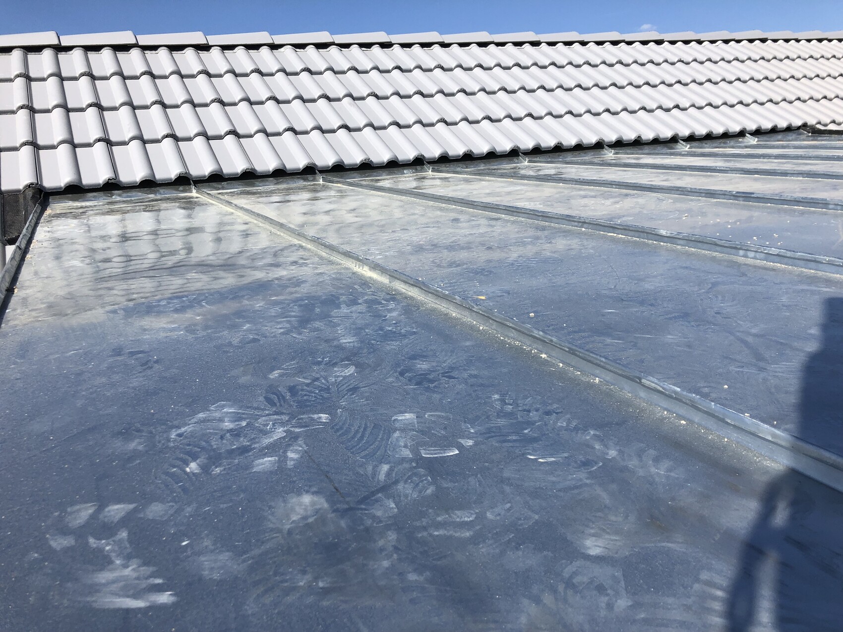 Ziegeldach über einem bläulich reflektierenden Flachdach; Spuren auf der Oberfläche und Schatten.
