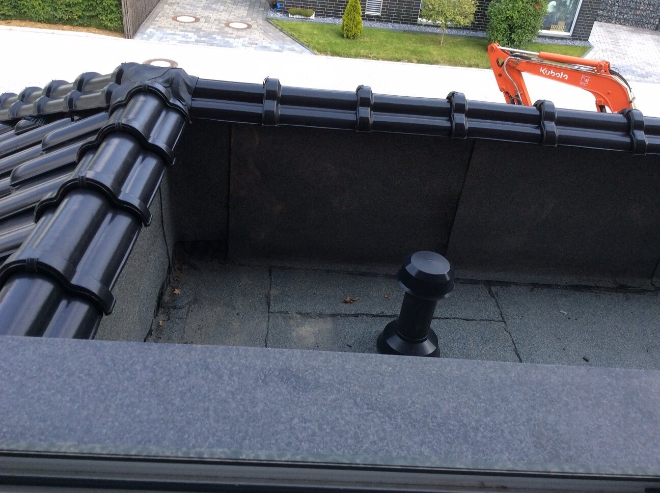 Dachkonstruktion mit schwarzen Ziegeln, Baugerät (orange Kubota) im Hintergrund