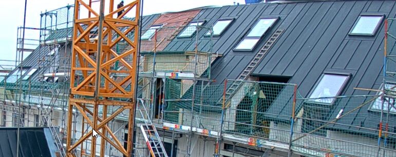 Baustelle mit Gerüst, orange Turmkran, Dachfenstern und Bauarbeiten auf Etagen