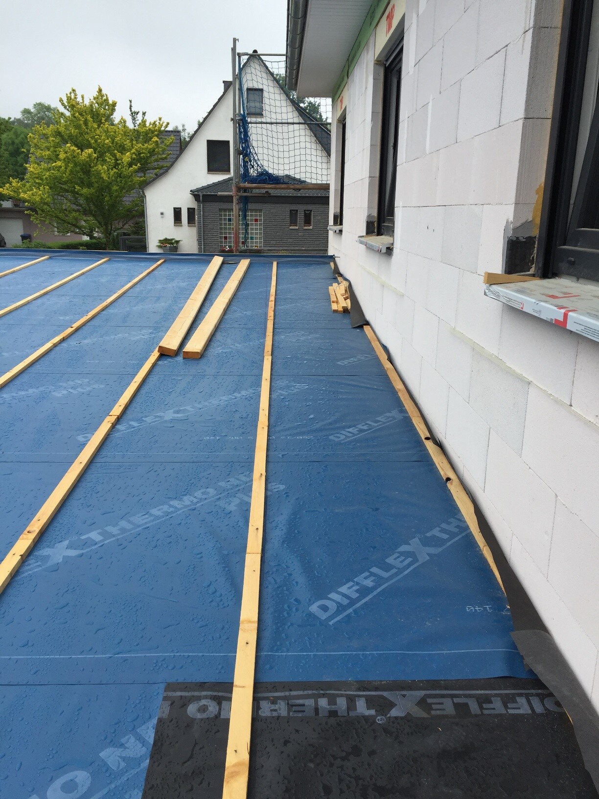 Dacharbeiten auf einem Haus mit blauer Dachbahn, Holzlatten installiert