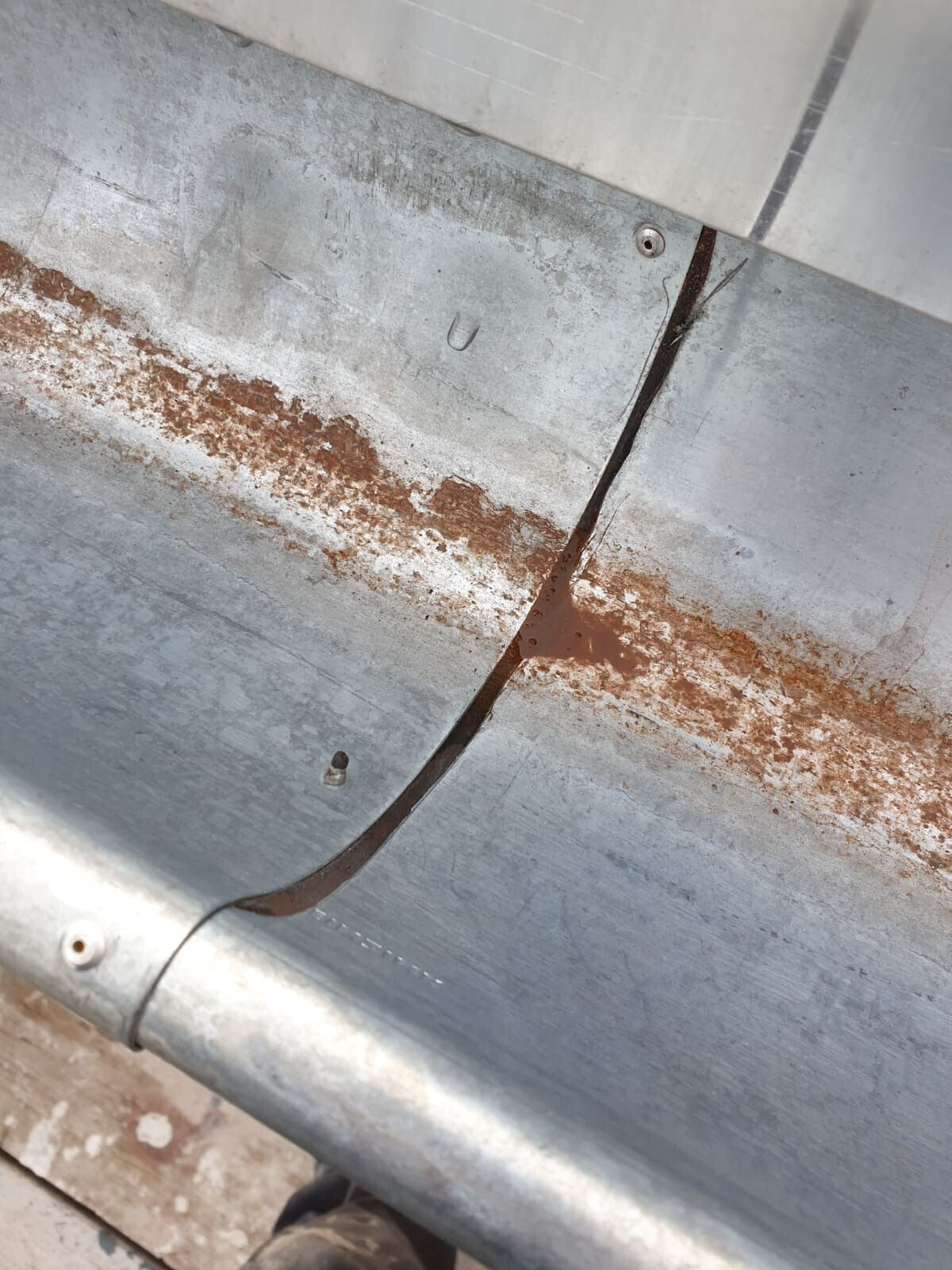 Nahaufnahme eines Metallblechs mit Rostflecken entlang einer Fuge und Schraubenköpfen.