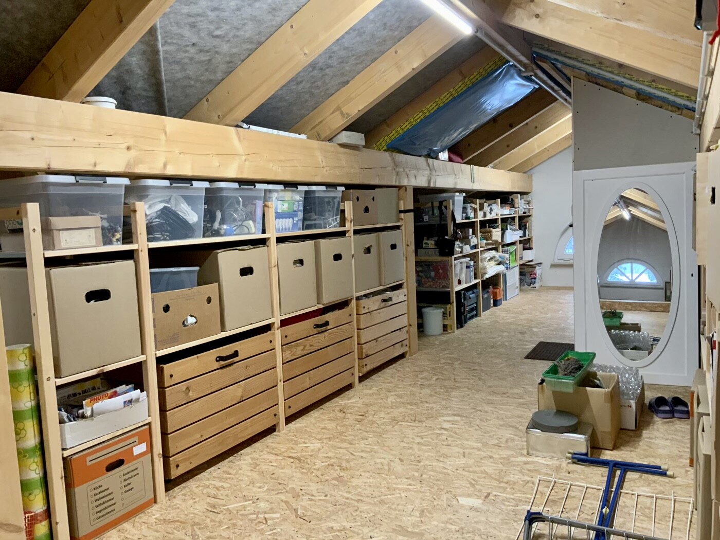 Dachboden mit langen Holzregalen, vielen Aufbewahrungsboxen, Kartons und Kisten unter Holzsparren.