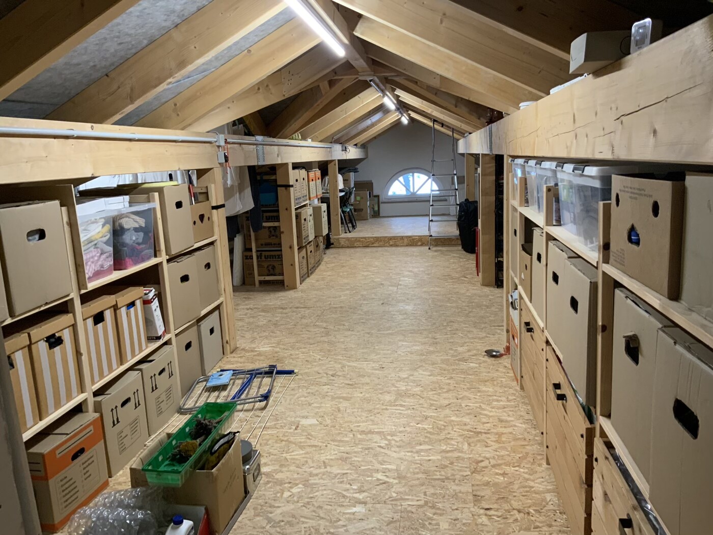 Dachboden-Lagerraum mit Holzbalkenregalen, Kartons und Boxen, Leiter im Hintergrund