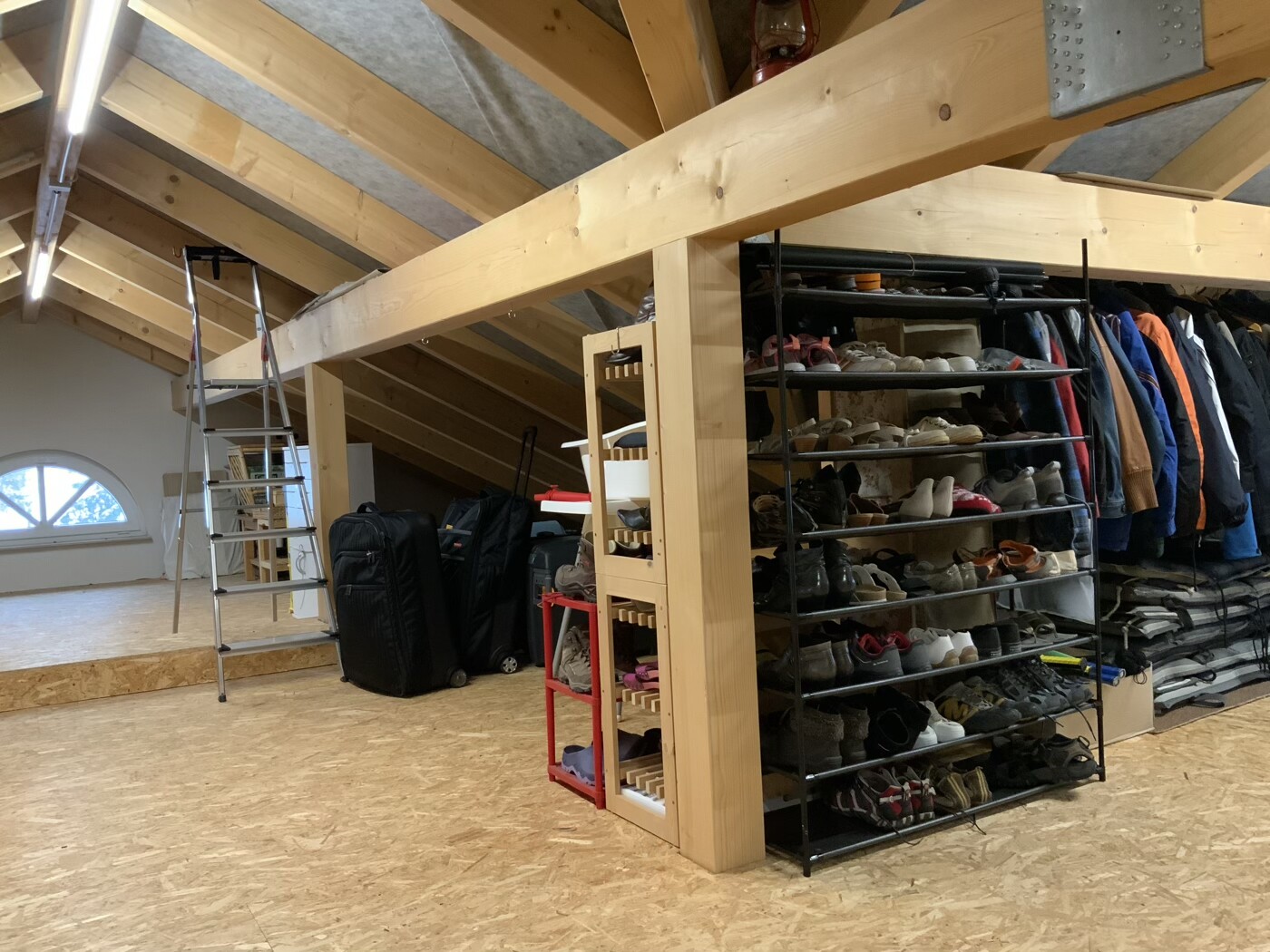 Heller Dachboden mit Holzbalken, Leiter, Schuhregal voller Schuhe, Jacken und Gepäck