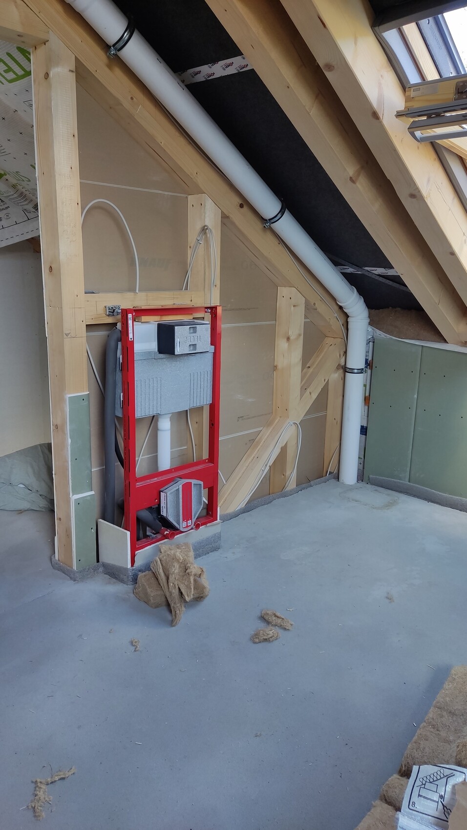 Roter WC-Trägerrahmen mit grauem Spülkasten und Abflussrohren im Dachgeschoss.