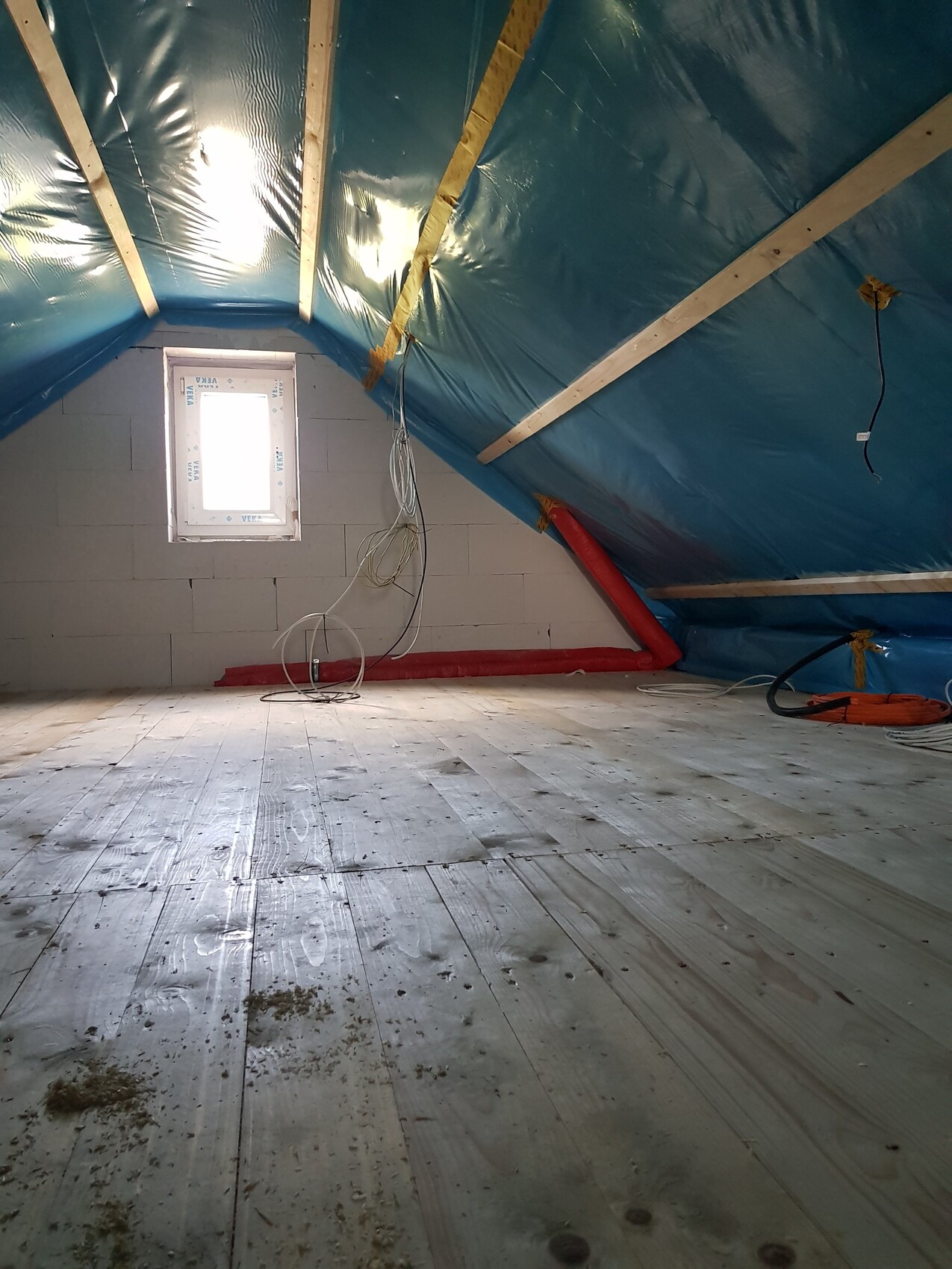 Dachboden-Baustelle: blaues Plastikdach, Holzbalken, lose Kabel, kleines Fenster, Holzboden.