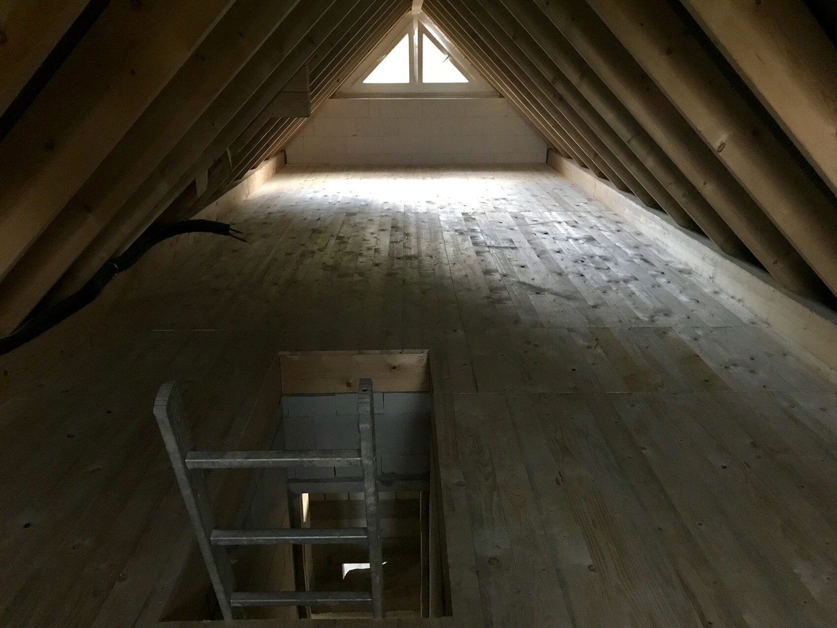Dachboden mit Holzbalken, Holzboden, Leiteröffnung im Boden und Licht am Ende