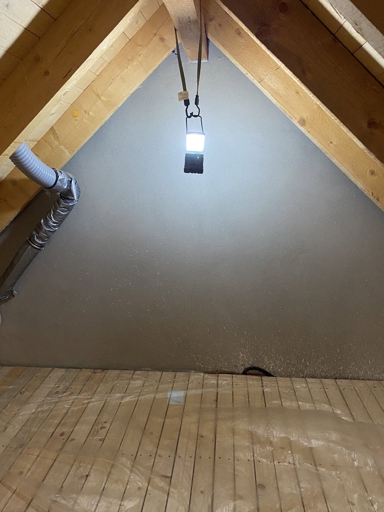 Dachboden mit sichtbarem Dachstuhl aus Holzbalken, Lüftungsschlauch und Arbeitslampe