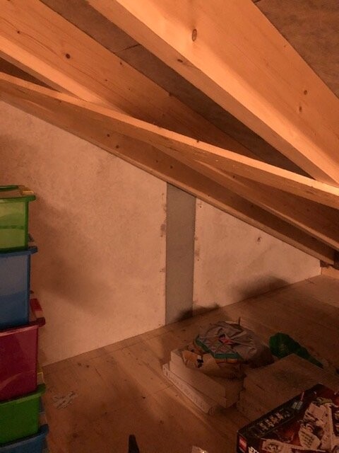 Dachboden mit geneigtem Holzbalken-Dach, links bunte Kunststoffboxen, Boden mit Papieren und Kartons.