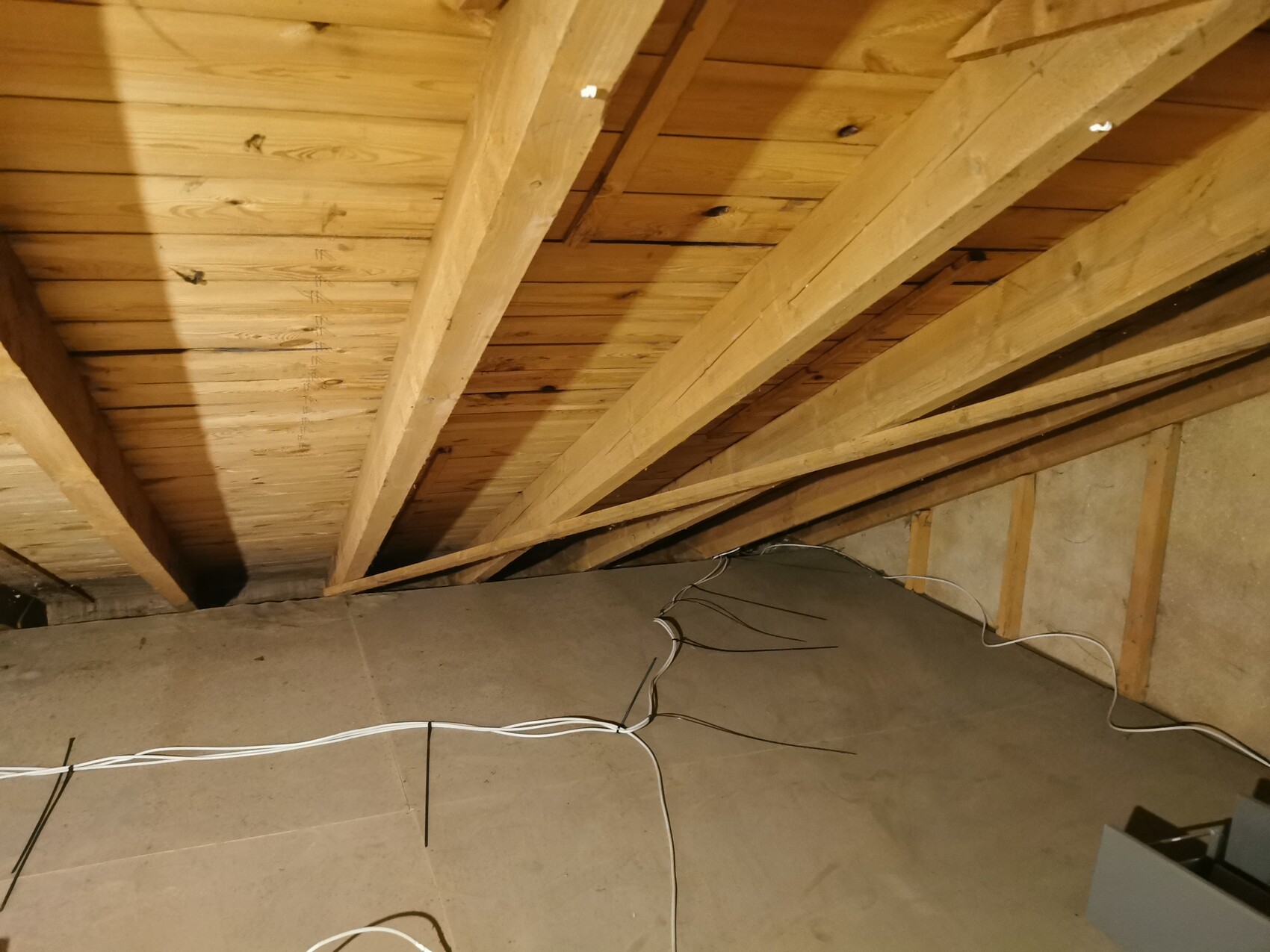 Unbearbeiteter Dachboden mit Dachstuhl aus Holzbalken und sichtbaren Kabeln