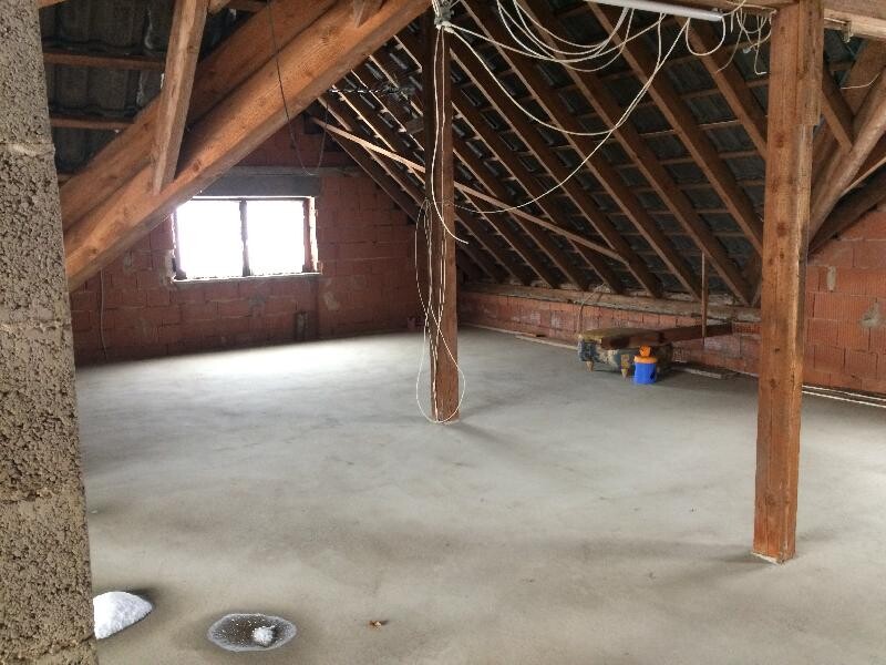 Dachboden mit Holzbalken, Kabeln von der Decke, Backsteinmauer, Fenster links, Werkzeug.