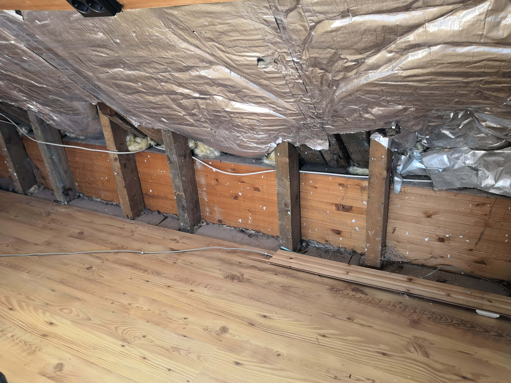 Dachboden: freiliegende Holzbalken, Dämmung zwischen den Balken, Folienverkleidung und Holzboden.