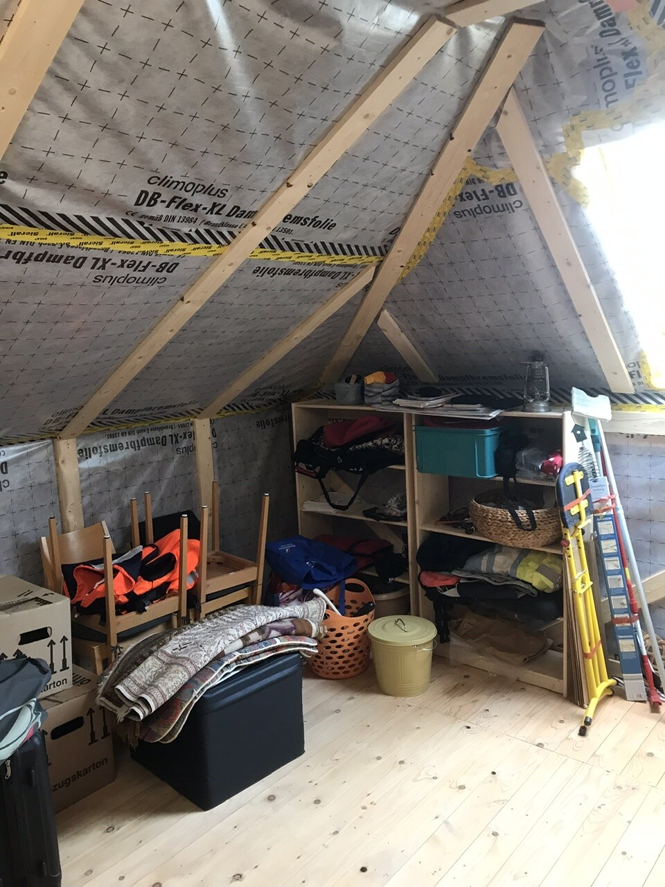 Dachbodenabstellraum mit Holzbalken, Dämmung an der Decke, Regale voller Kleidung und Körben.