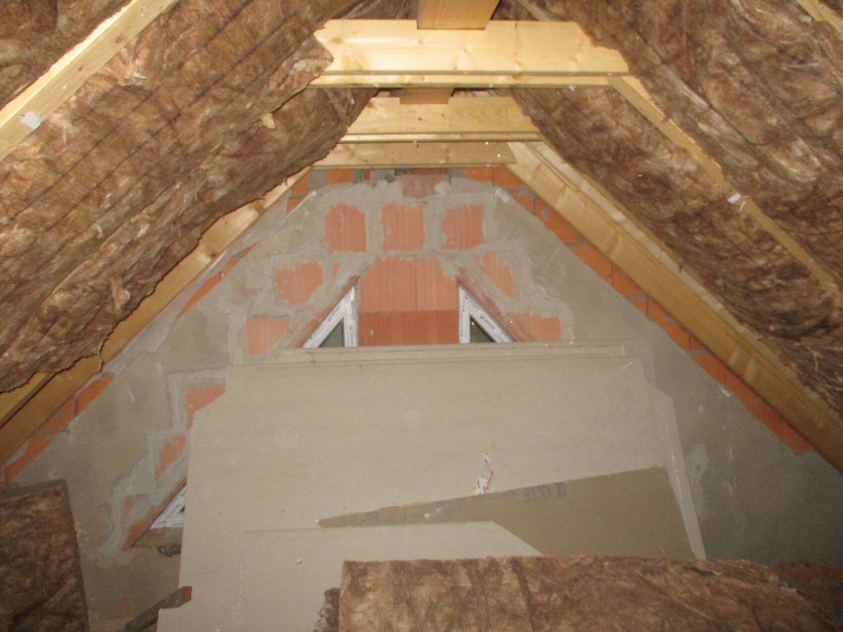 Dachboden im Rohbau mit Dämmung, Holzbalken und Ziegelwand im Giebel.