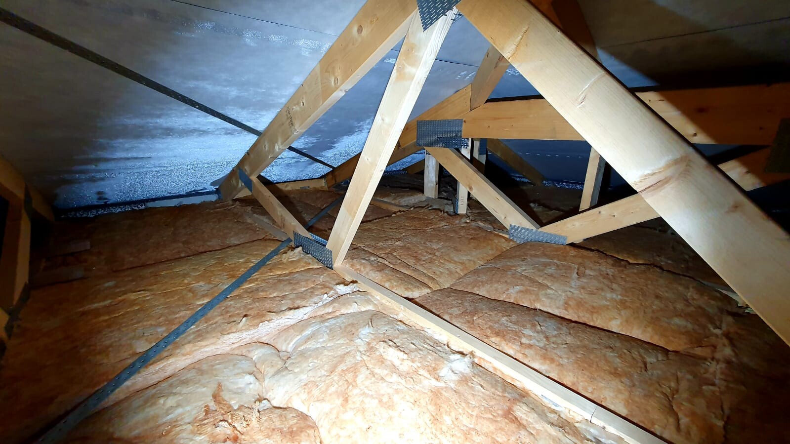 Dachboden mit sichtbaren Holzbalken, Dämmwolle auf dem Boden und Folien-Dämmung an den Wänden.