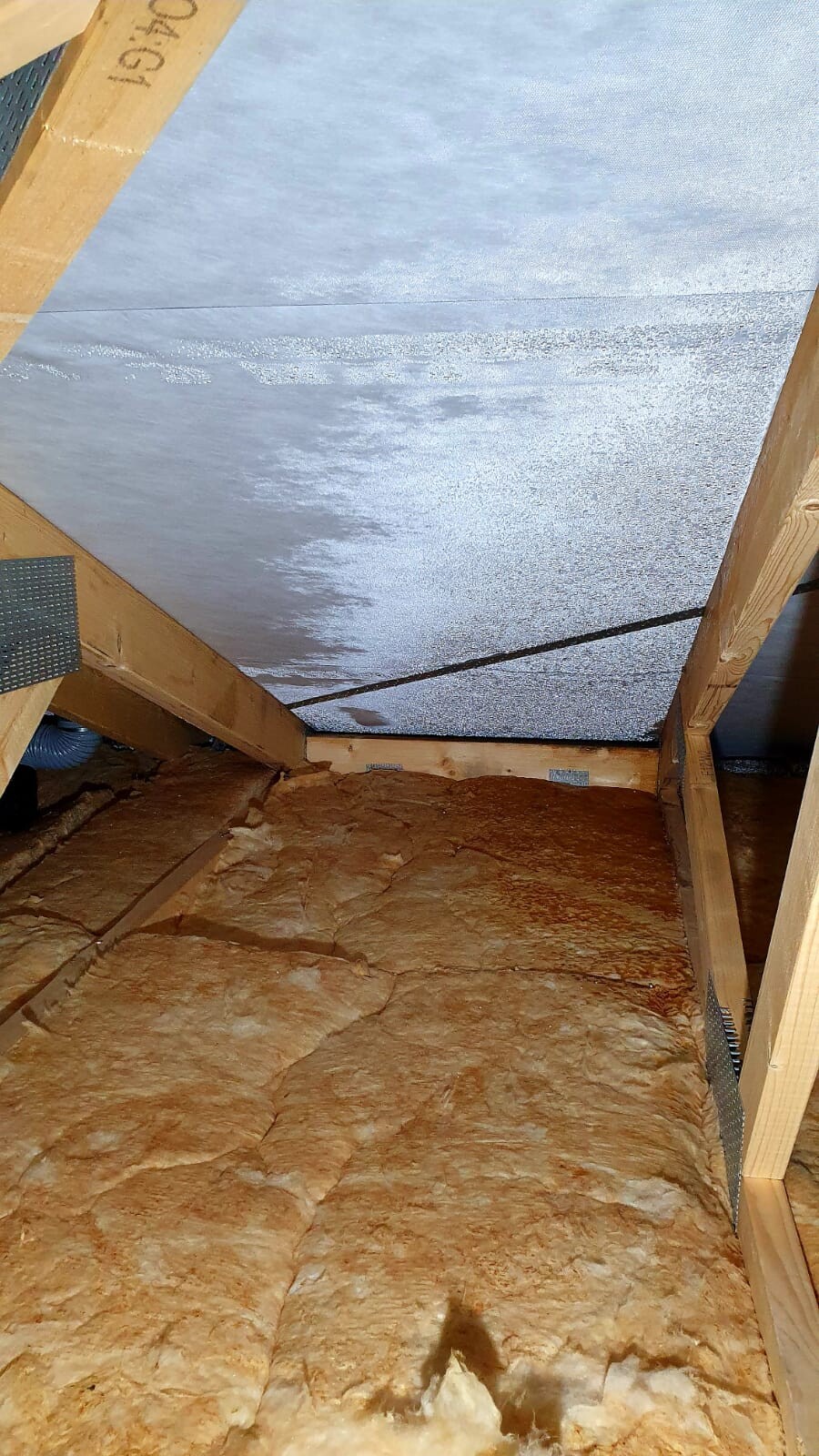 Dachboden mit Holzbalken, silberne Dämmplatten an der Dachkonstruktion und braune Isolierwolle auf dem Boden.