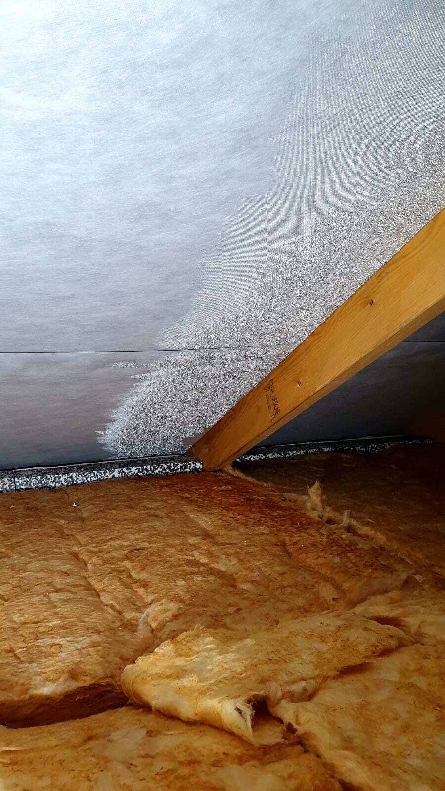 Dachboden: braune Glaswolle-Isolierung auf dem Boden, diagonaler Holzbalken, graue Dachverkleidung.