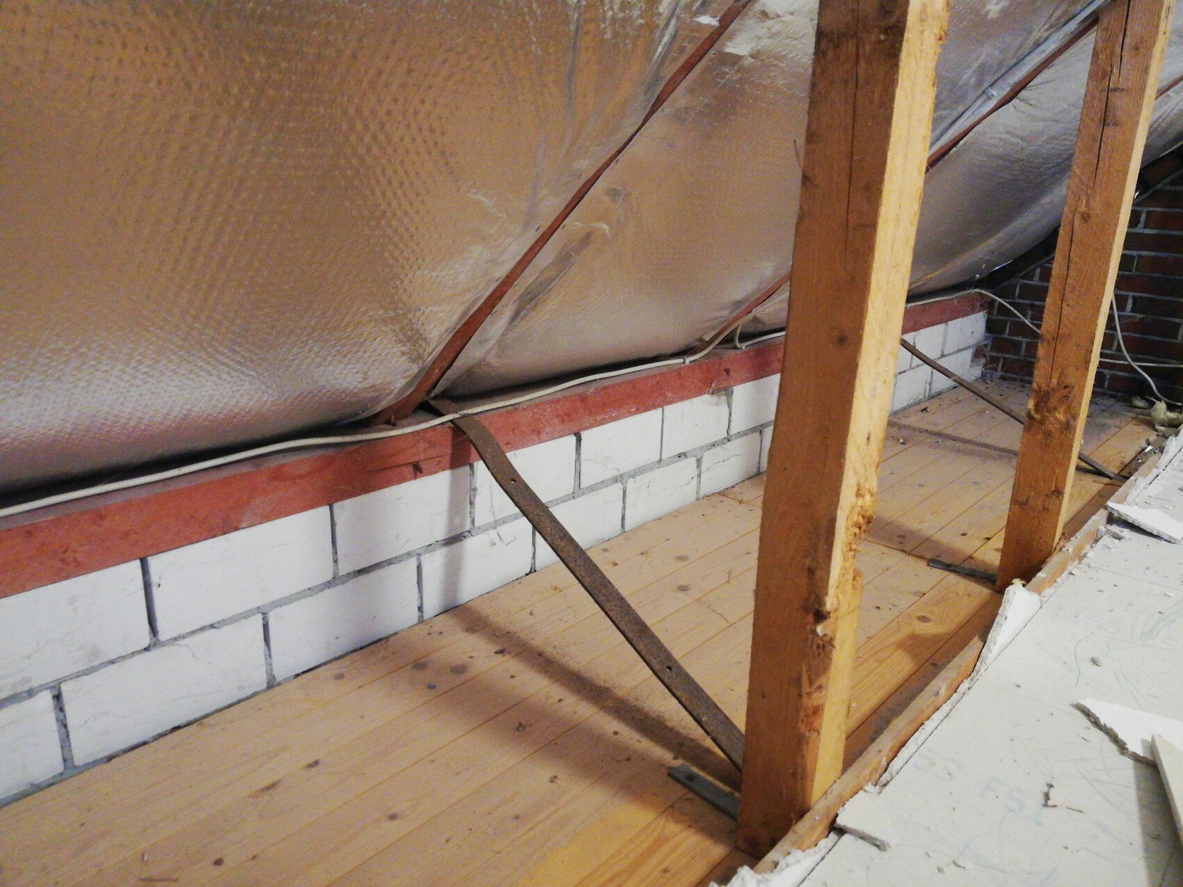 Dachboden mit Dämmfolie, Holzständern, diagonaler Metallstrebe und Holzboden.